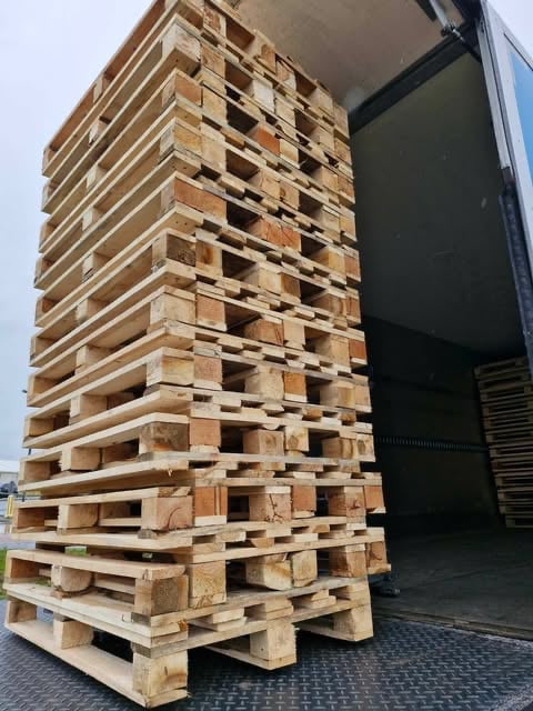 Stacked wooden pallets forming a tall tower structure next to a black truck bed