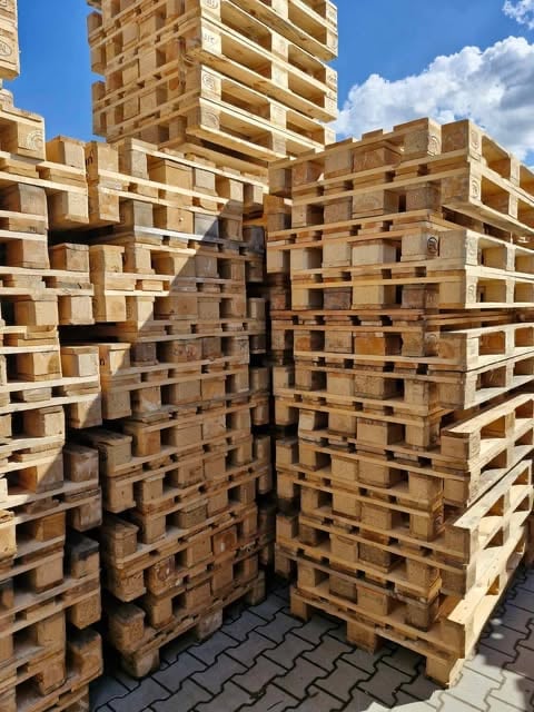 Stacked wooden pallets creating a corridor-like formation on pavement under blue sky