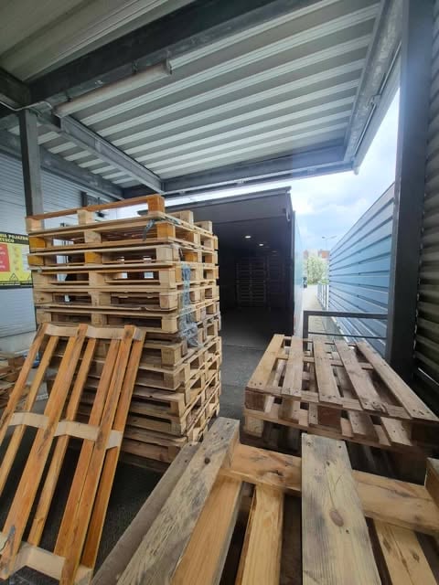 Interior of storage unit with stacked wooden pallets, metal roof, and open doorway revealing sky