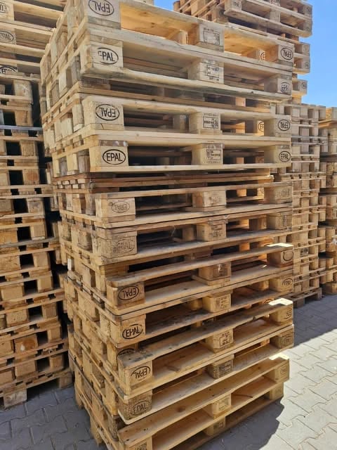 Stack of wooden EPAL pallets marked with logos, arranged in rows outdoors with clear blue sky background