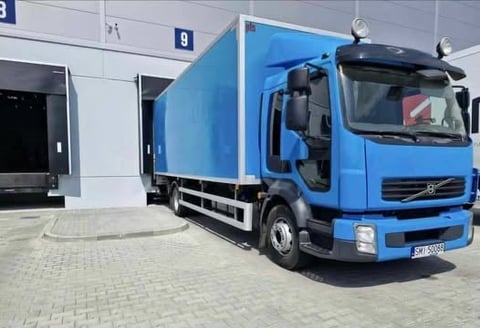 Blue Volvo delivery truck parked in front of a warehouse with white and gray exterior